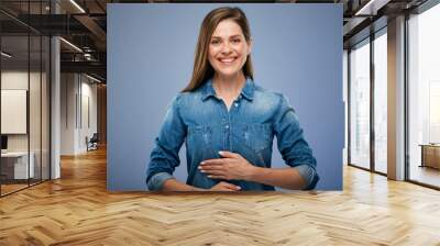 Smiling happy woman in blue shirt holding hands on stomach. isolated portrait on blue studio background. Wall mural