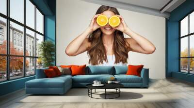 Smiling woman holding two half og oranges fruit ahead of eyes. Wall mural