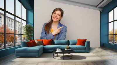 Smiling woman in blue business suit pointing finger at side, isolated female portrait. Wall mural