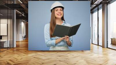 Student woman architect or engineer holding book wearing safety industrial helmet. Isolated female portrait. Wall mural