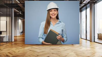 University engineering student wearing protective industrial helmet with a book in her hand. Isolated female portrait.. Isolated female portrait. Wall mural