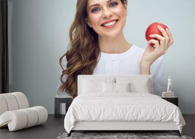 woman with toothy smile wearing white shirt holding red apple. Wall mural