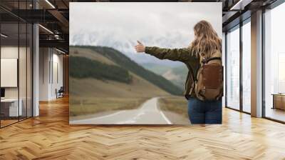 A woman with a backpack and a road stretching into the distance against the backdrop of mountains Wall mural