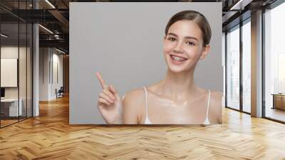 Lovely girl in braces smiling and pointing at the empty space Wall mural