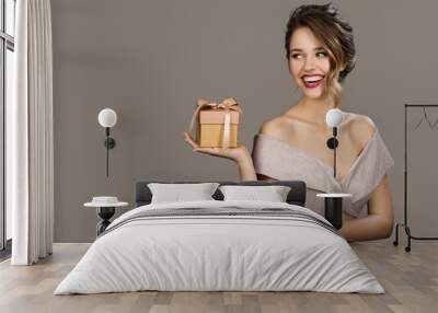 Portrait of smiling pretty woman holding a gift box in hands. Gray background. Wall mural