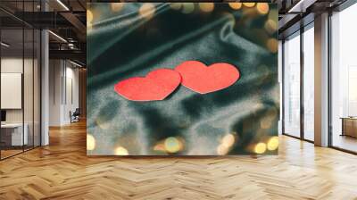 two red hearts on a black silk background. Beautiful bokeh effect from a garland. Wall mural