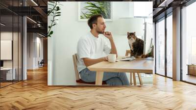 Confident man read business email on computer working from home office during coronavirus lockdown with cat sit on desk. Busy worker at workplace. Remote or freelance occupation on covid-19 quarantine Wall mural