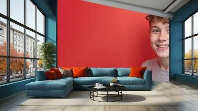 Smiling teenage boy with cheerful expression against vibrant red background with copy space Wall mural