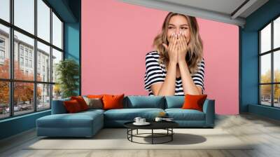 Surprised young woman excited cover open mouth and look side happy laughing over pink studio wall. Young blonde female amazed with happiness in positive shock cheering to good amazing news isolated Wall mural