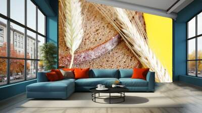 Two pieces of rye bread and rye spikes are located on a yellow background Wall mural