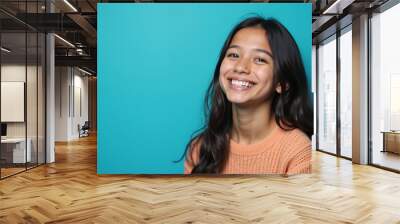 Young woman with radiant smile posing against vibrant turquoise background with copy space Wall mural