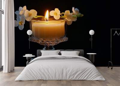 Burning white candle glowing in a glass candlestick, surrounded by flowers, isolated on a black background Wall mural