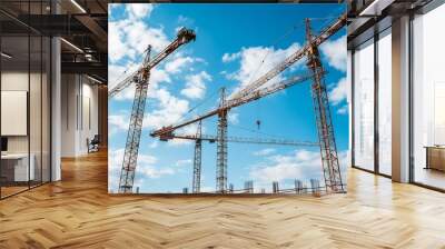 Construction cranes stand tall against the blue sky at a construction site. Wall mural