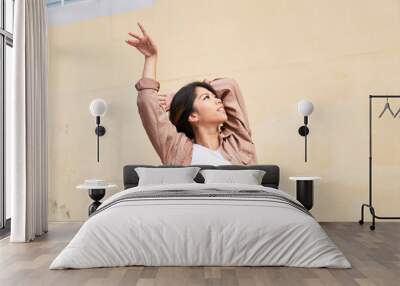 Woman dancing in front of beige wall with arm behind head and hand raised Wall mural