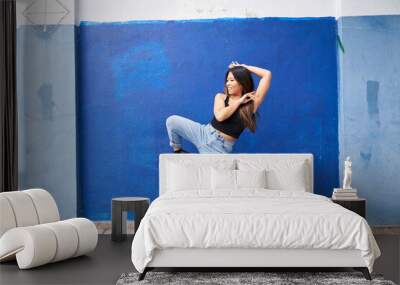 Woman dancing in front of blue wall outdoors kicking Wall mural