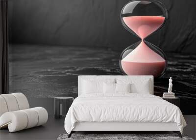 A close-up of an hourglass with pink sand on a dark surface. Wall mural