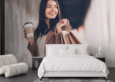 Beautiful fashionable woman with shopping bags and coffee walking near mall. Wall mural