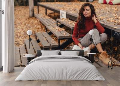 Beautiful woman in cozy outfit reading book sitting on wooden bench in autumn park. Wall mural