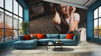 Happy smiling woman in glasses sitting on wooden steps in street. Wall mural