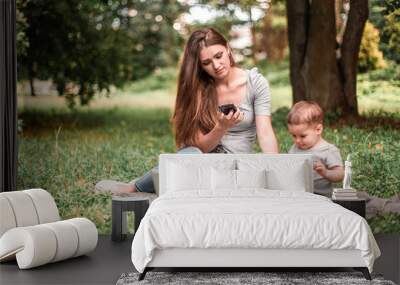 Mother with son sitting in the park, using phone and work on laptop. Wall mural