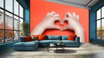 Child make a heart on a red background. Wall mural