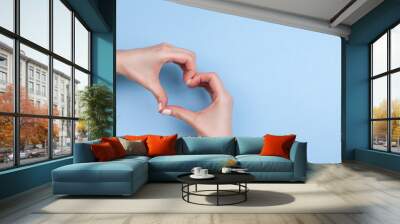 Female hands show a heart symbol on a light blue background. Place for text. Wall mural