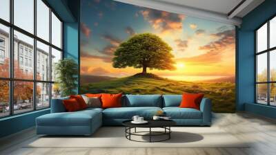 A lonely tree surrounded by lush green grass under the warm glow of a cloud-filled sunset sky Wall mural