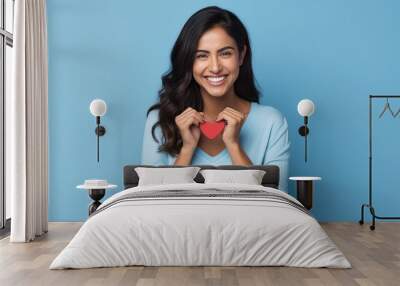 Hispanic woman standing over blue background smiling lovingly and making heart symbol shape with hands. romantic concept. I love you. Valentine's day  Wall mural