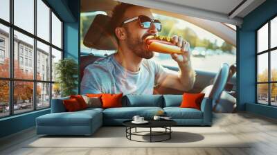 Man is operating a car while eating a hot dog and a cold beverage in a risky manner. Wall mural