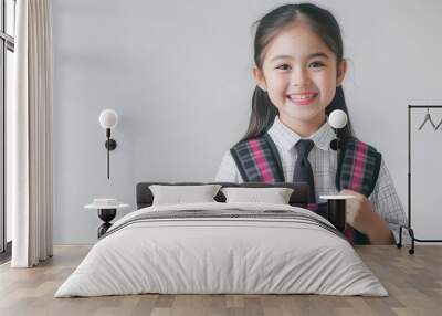 Smiling girl in a dress shirt and tie wears a plaid backpack, showcasing excitement for school in a bright indoor setting Wall mural