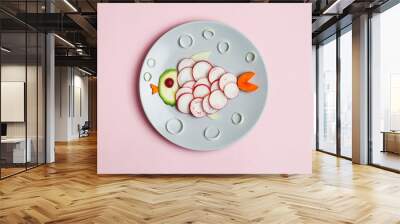 food art, creative children breakfast, cute funny fish made of colorful fresh tasty vegetables, carrot, zucchini, tomato, radish isolated on pastel pink background Wall mural