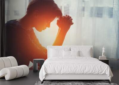 silhouette of young woman raising hands praying at sunset or sunrise light at home, religion and spirituality concept Wall mural