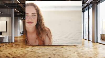 A young woman on a sandy beach with the ocean in the background, serene expression. Wall mural