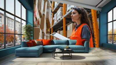 In an industrial jumpsuit, a stockroom supervisor searches parcels and checks postal forms. A shipping company worker supervises cardboard boxes and writes on a clipboard in a mail sorting center. Wall mural