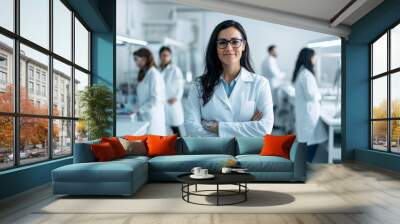 In modern medical science laboratory with Team of Specialists in background, young woman scientist wears white coat and glasses. Wall mural