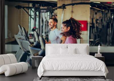 A fit sporty couple is running together on a treadmill in a gym during cardio training. Wall mural