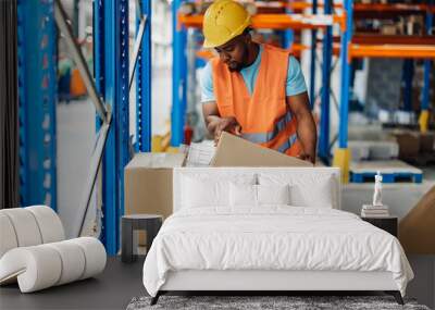 African american male warehouse worker handling box with care in stockroom aisle Wall mural