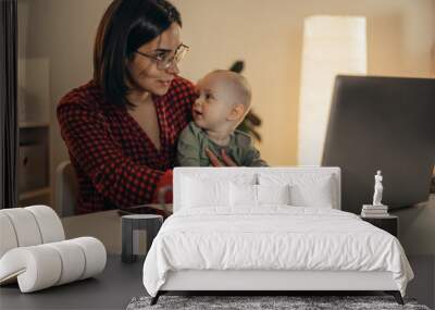 Beautiful business mom using a laptop and spending time with her baby boy at home Wall mural