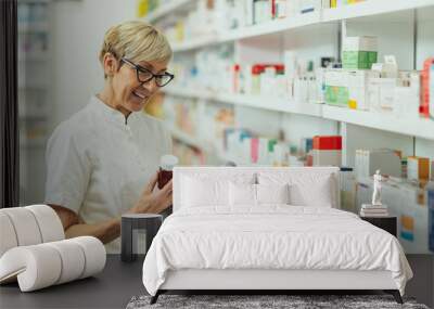 Beautiful senior female pharmacist checking medications on a shelf Wall mural