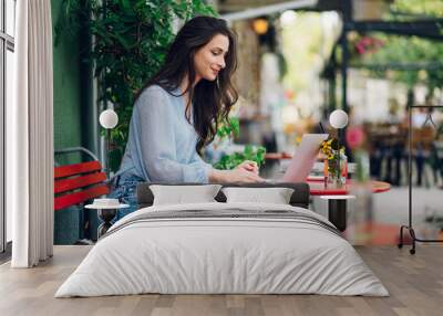 Beautiful woman sitting in a street cafe and using a laptop Wall mural