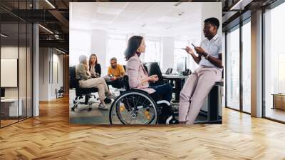 Businesswoman with disability listening to multiracial colleague at office. Wall mural