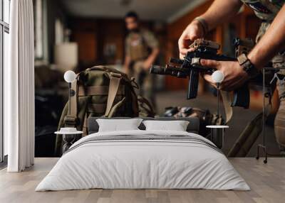 Close up of airsoft fighter's hands holding rifle and putting battery on Wall mural