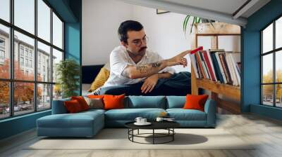 Fashionable hipster man with mustache reading a book while at home. Wall mural