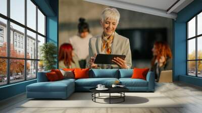 Happy mature female boss smiling at tablet at office during meeting. Wall mural