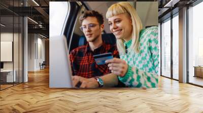 Happy passengers using laptop and credit card on a train during trip. Wall mural