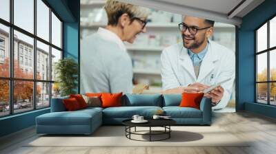 Male pharmacist selling medications at drugstore to a senior woman customer Wall mural