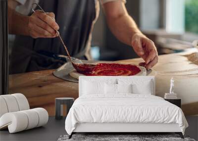 Man worker in a pizza place placing ingredients on pizza dough Wall mural