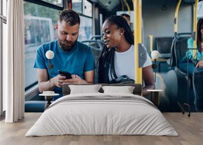 Multiracial friends talking and using a smartphone while riding a bus in the city Wall mural