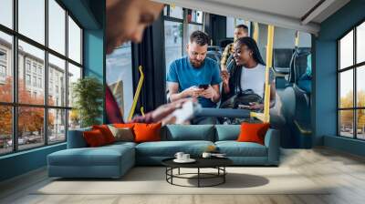 Multiracial friends talking and using a smartphone while riding a bus in the city Wall mural