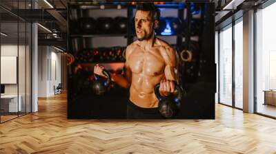 Muscular man holding kettlebells while training in a fitness gym Wall mural